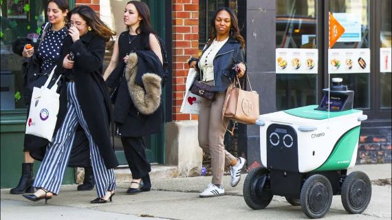 A delivery robot is seen on a busy pavement